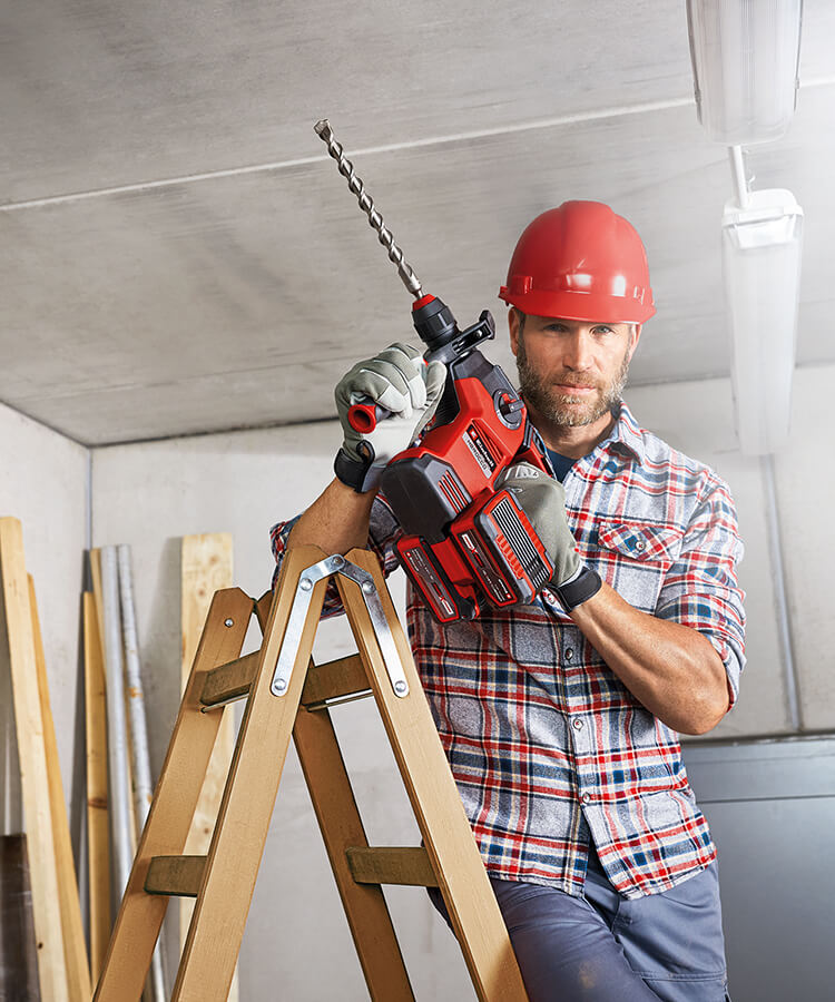 A man stands on a ladder with a hammer drill in his hand